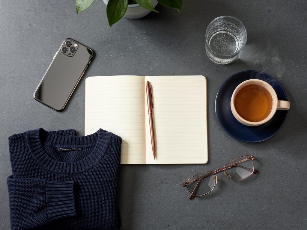 Photorealistic top-down flat lay on a slate-grey counter in soft even indoor light showing the things of an ordinary day